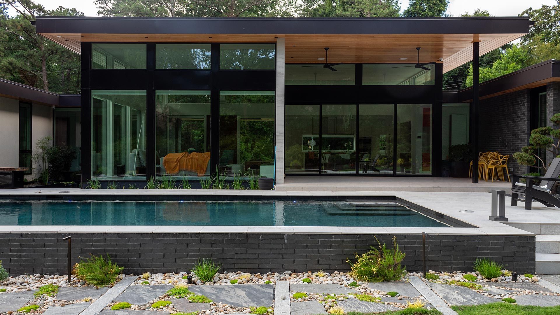 Modern glass-front house with a pool and stone patio in front