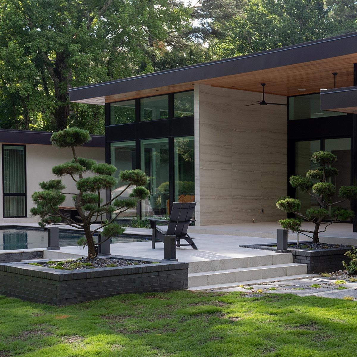 Modern house with landscaped courtyard, trimmed trees, and a patio chair near large windows