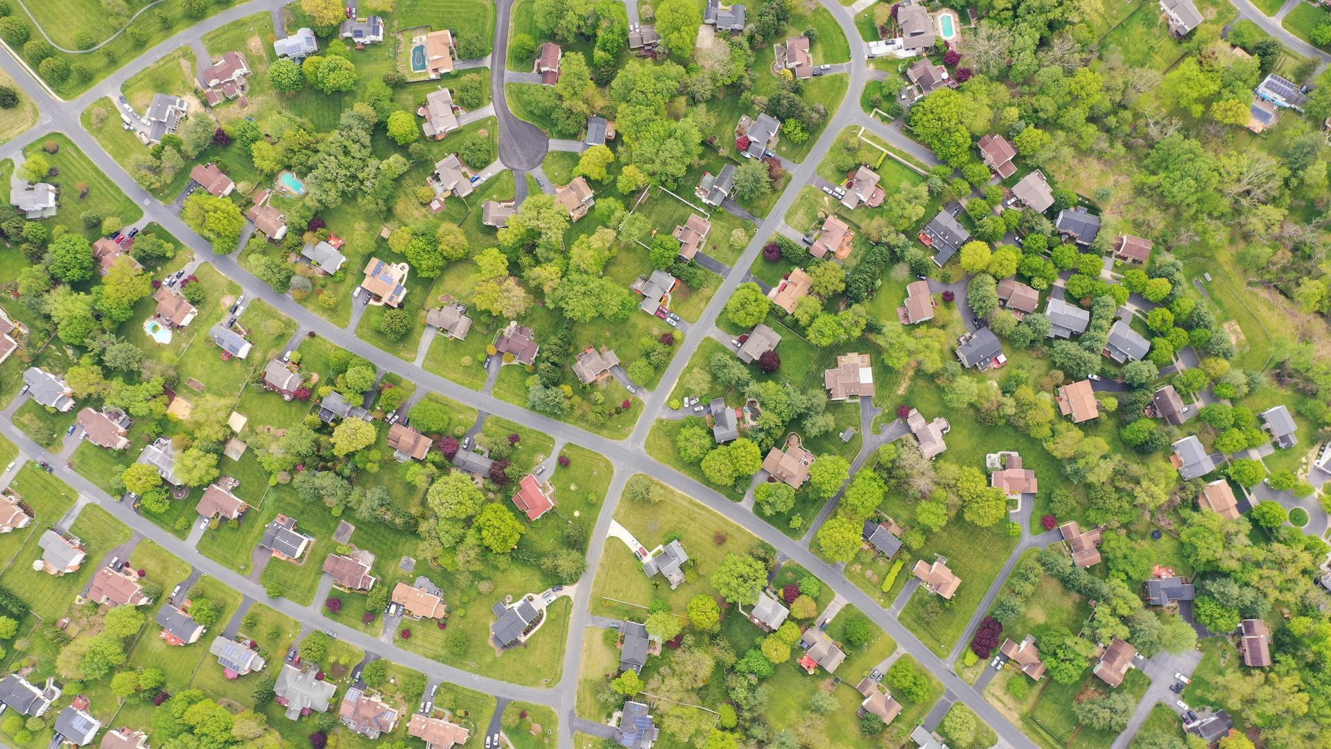 Aerial view of a suburban neighborhood with houses, roads, and dense green trees.