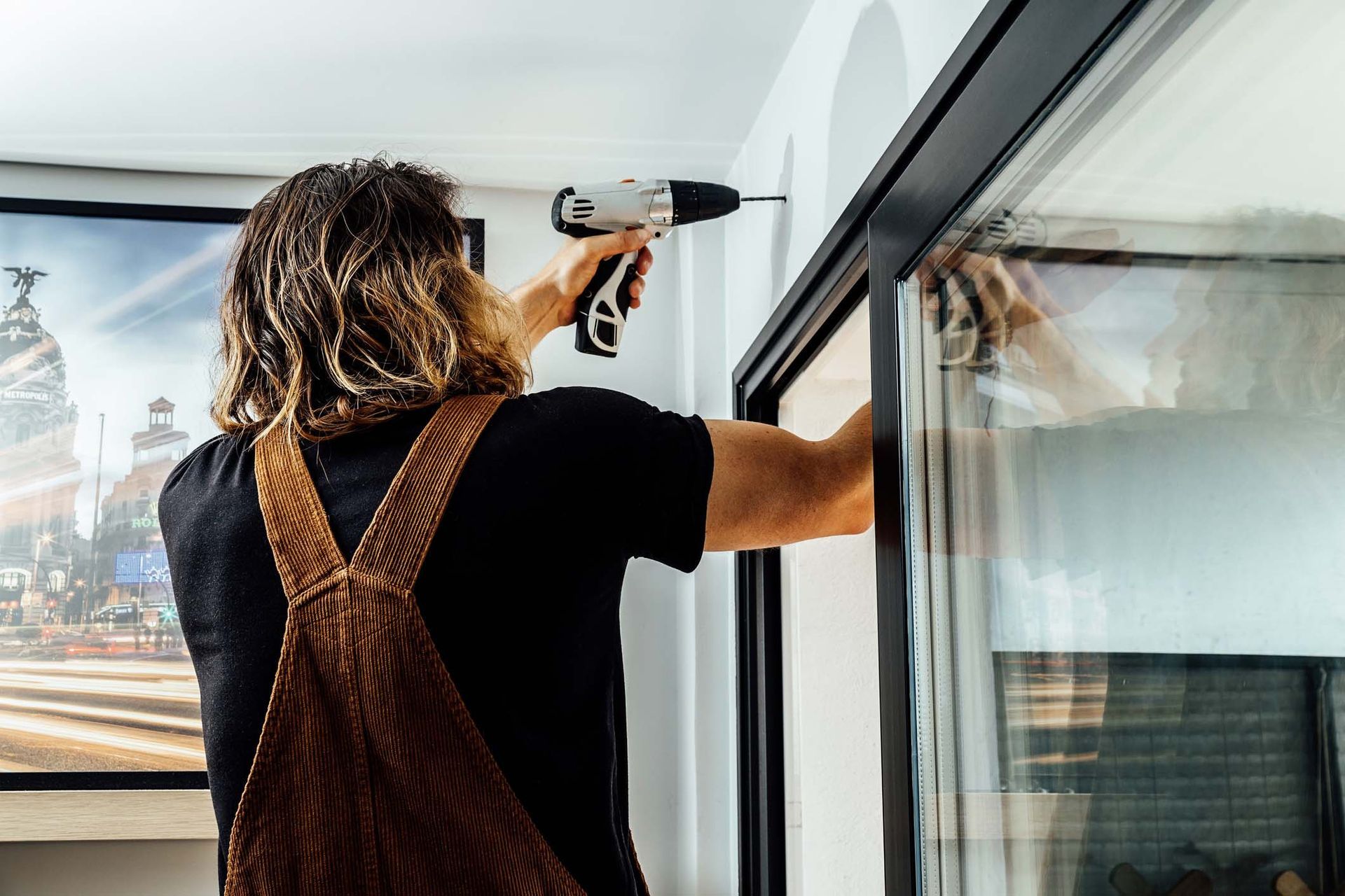 A man is using a drill to fix a window.