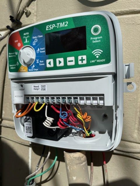 A green and white ESP-TM2 irrigation controller mounted on a wall with various colored wires connected.