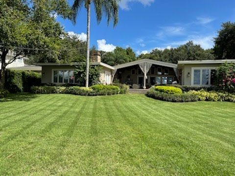 A one-story house with a green lawn and manicured bushes under a blue sky.