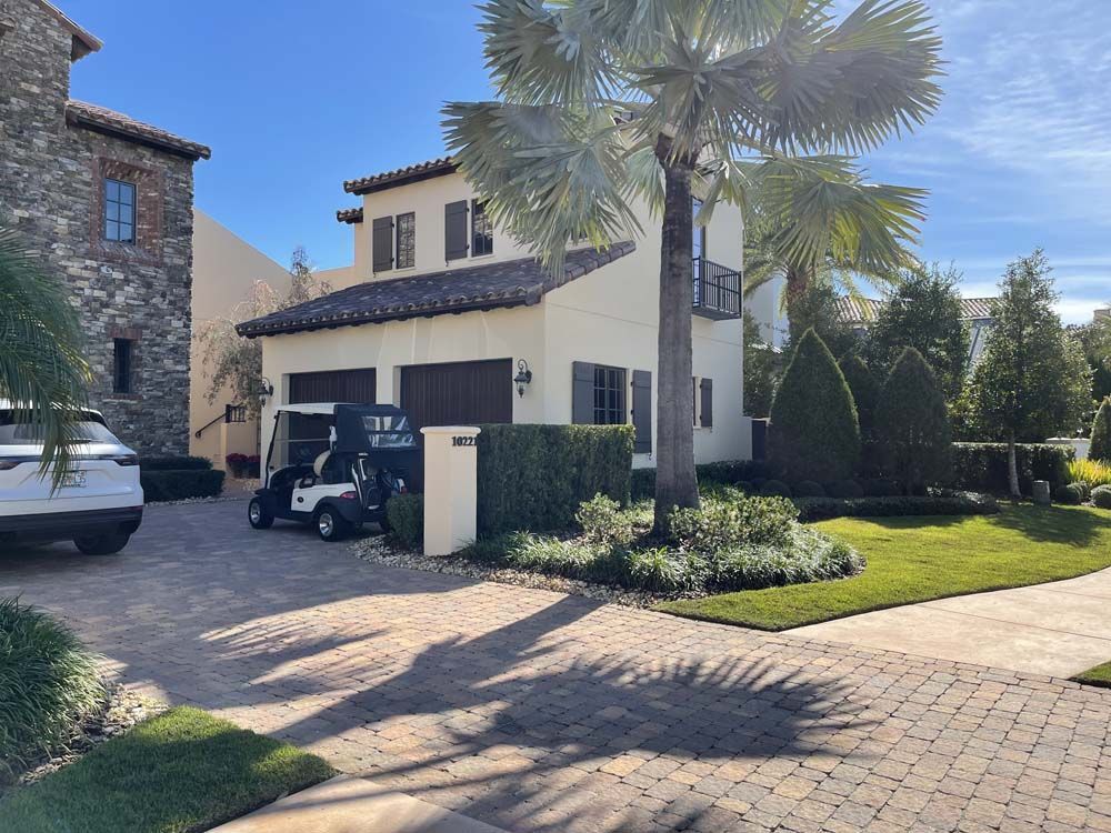 Beige stucco house with brown garage doors, golf carts, and palm trees. Sunny day.