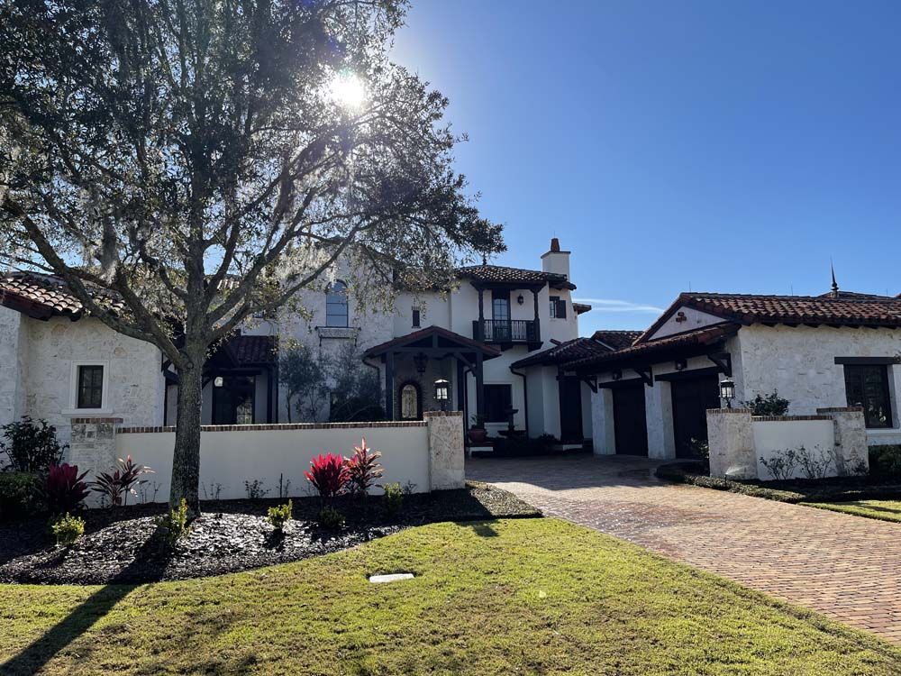 Spanish-style house with white stucco walls, red tile roof, and a sunny blue sky.