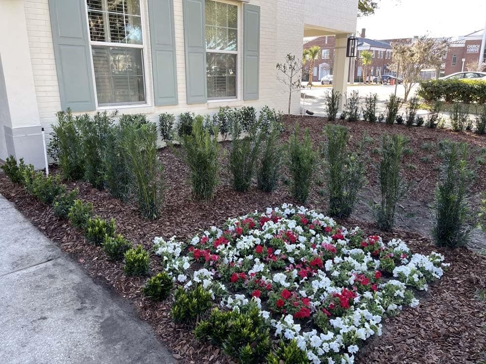 Exterior landscaping with trimmed bushes, flowers, and building with shutters.