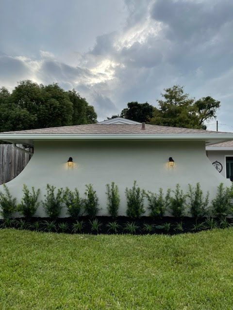 White building with two wall lights, shrubs, and a green lawn under a cloudy sky.