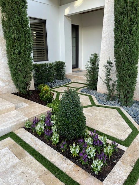 Landscaped front yard with pathways, stone planters, greenery, and tall cypress trees.