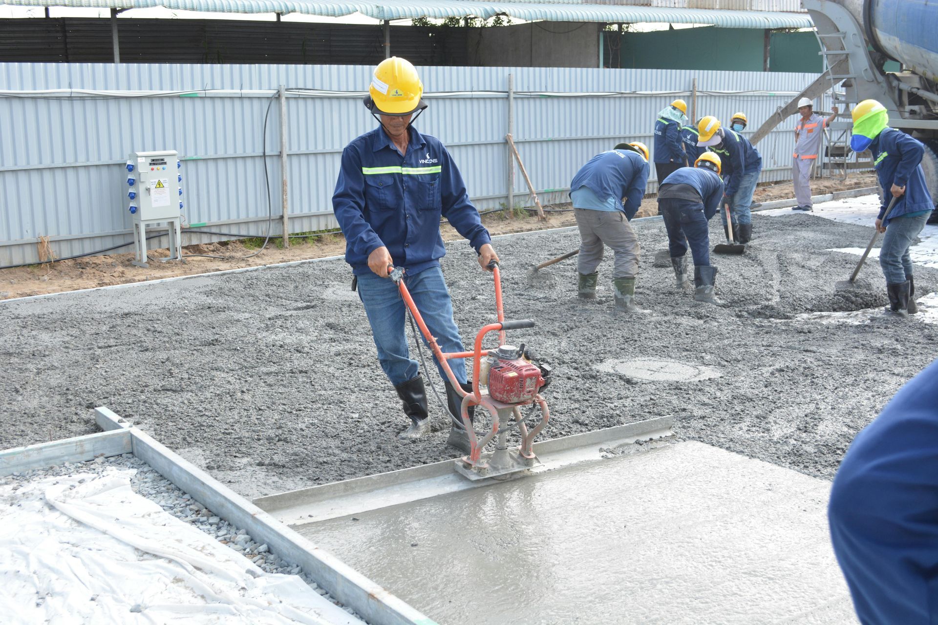 Workers using a power trowel to finish wet concrete at a construction site