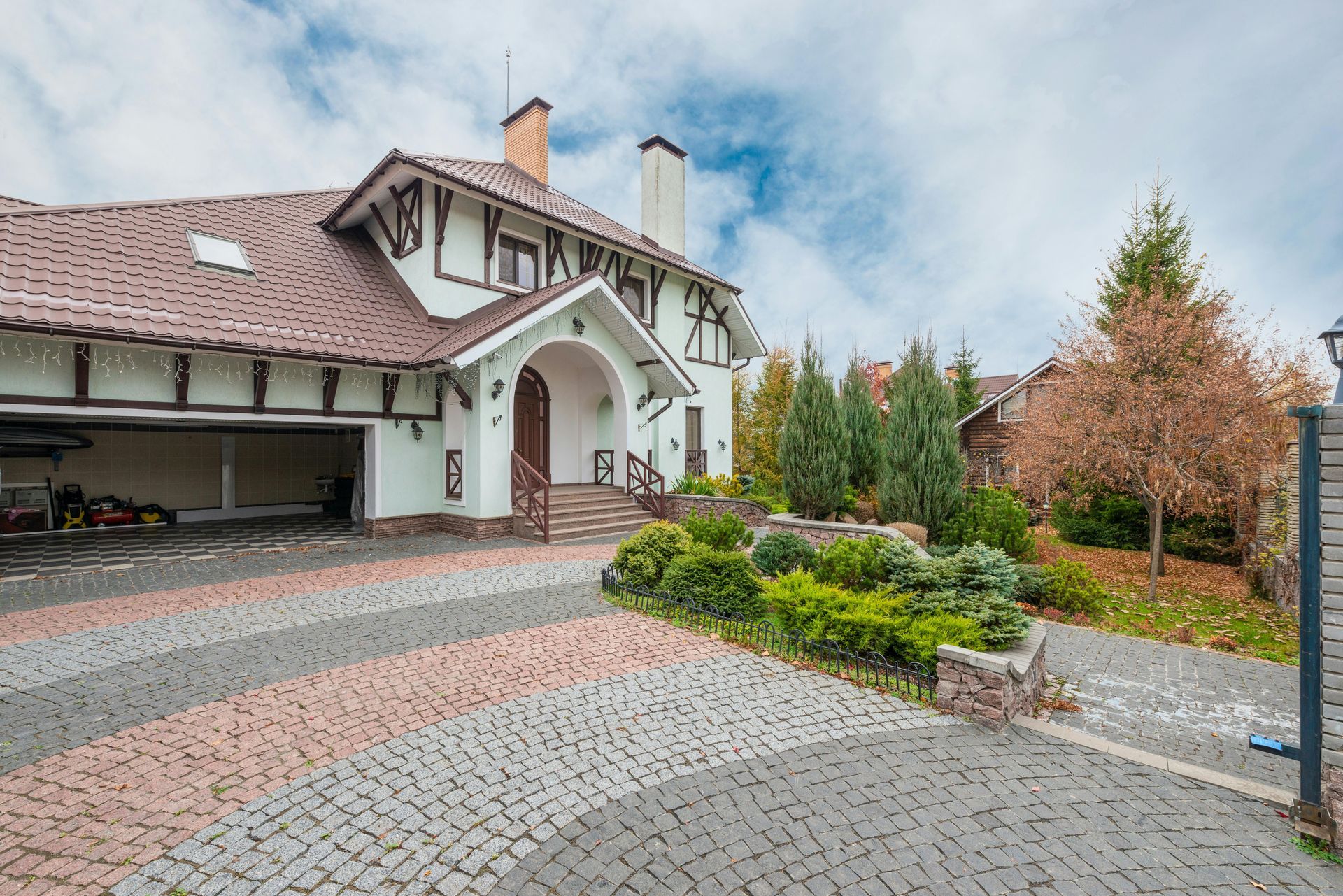Large house with tiled roof, arched entry, and landscaped driveway under a cloudy sky