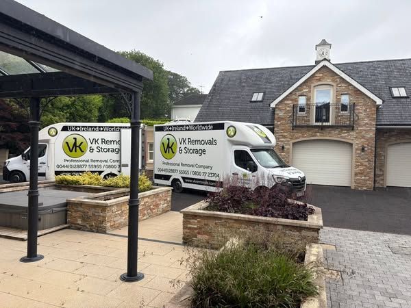 Two white moving vans parked in front of a large brick house.
