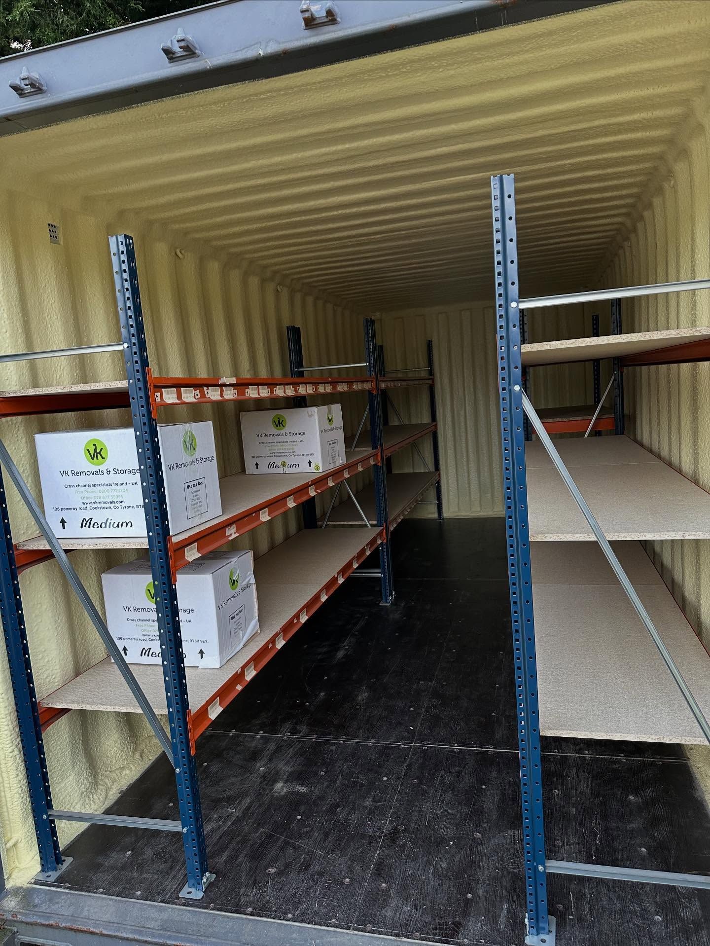 Inside a shipping container: metal shelving with boxes and bare shelves.