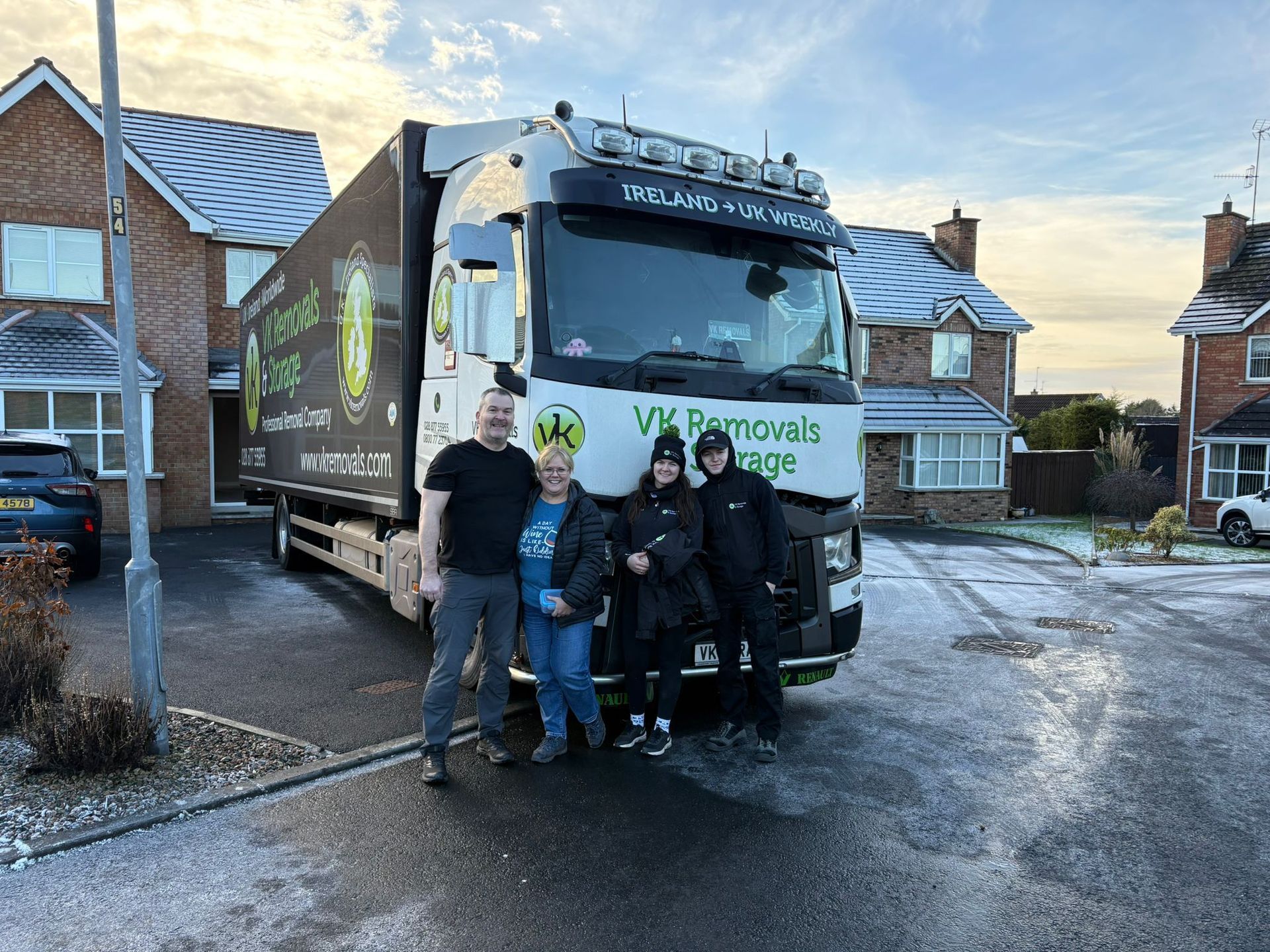 A family stands in front of a moving truck in a snowy residential area, ready to move.