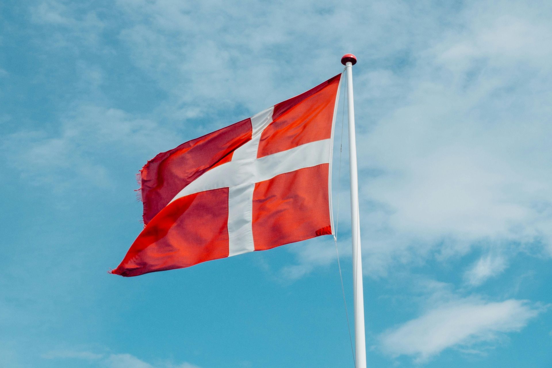 Danish flag, red with white cross, waving in the breeze against a blue sky.