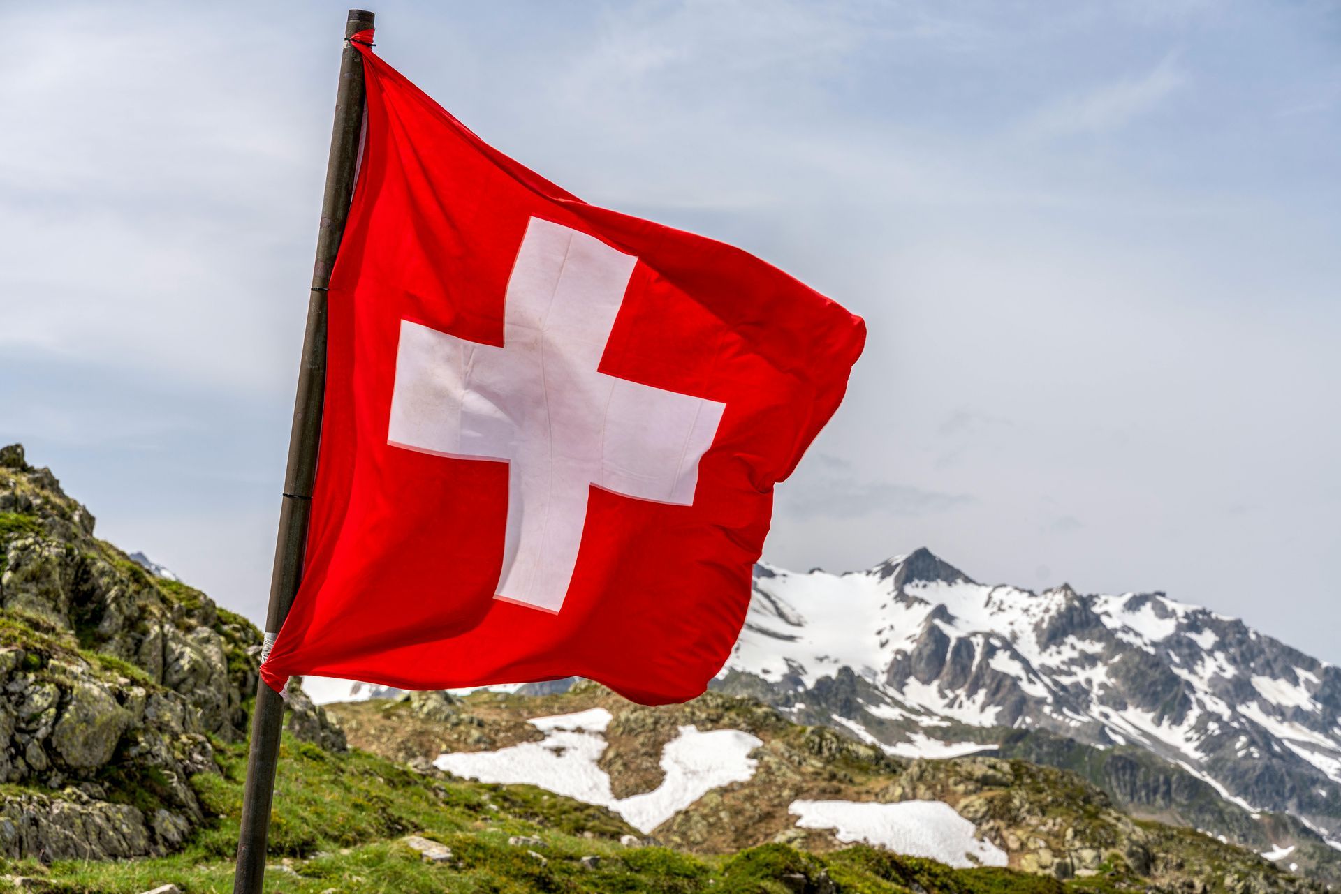 Swiss flag waving with snow-capped mountains in the background.