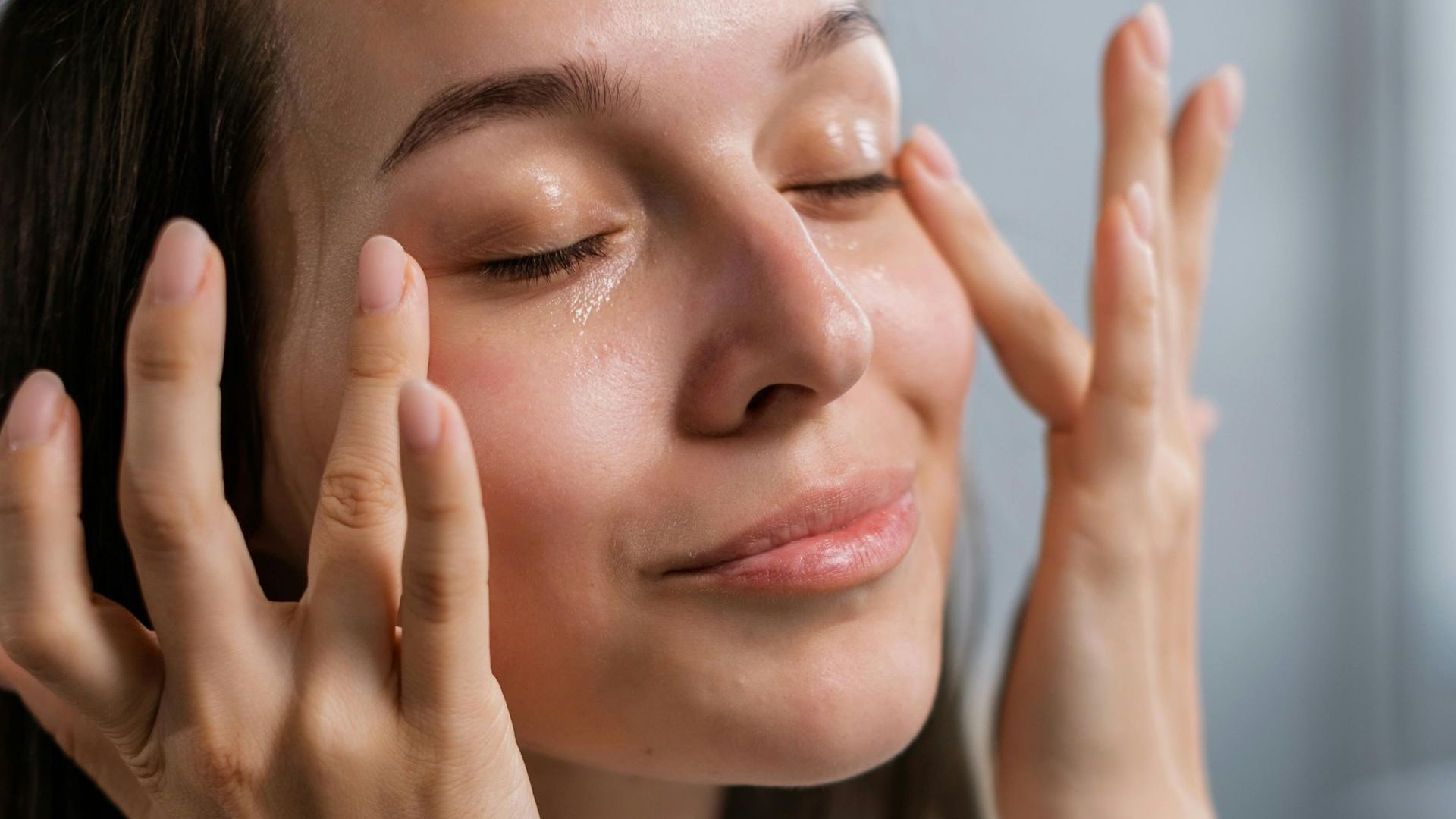 A woman is washing her face with her hands.