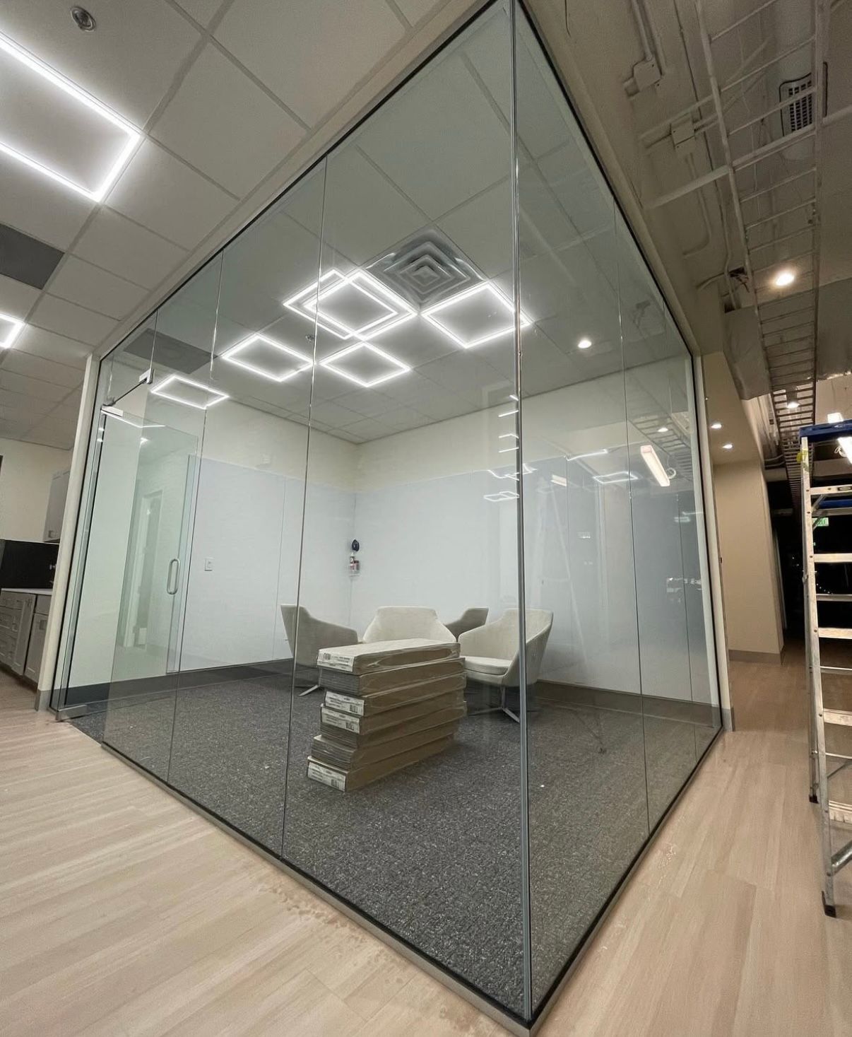 Glass-walled office space with seating, modern lighting. Gravel flooring, wooden floor outside.