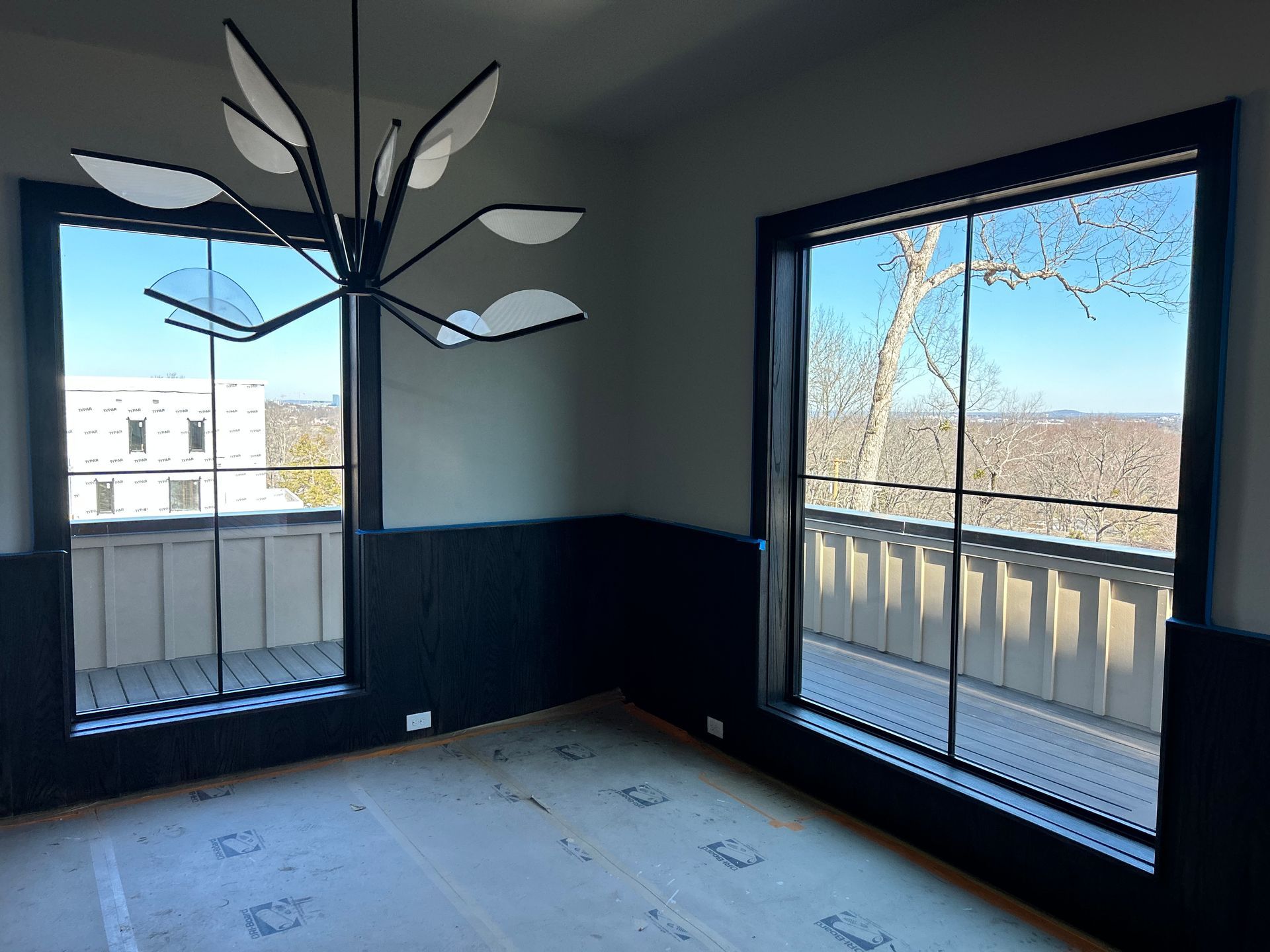 Room with two large windows and a modern chandelier; black trim on the windows and walls; view of trees and sky.