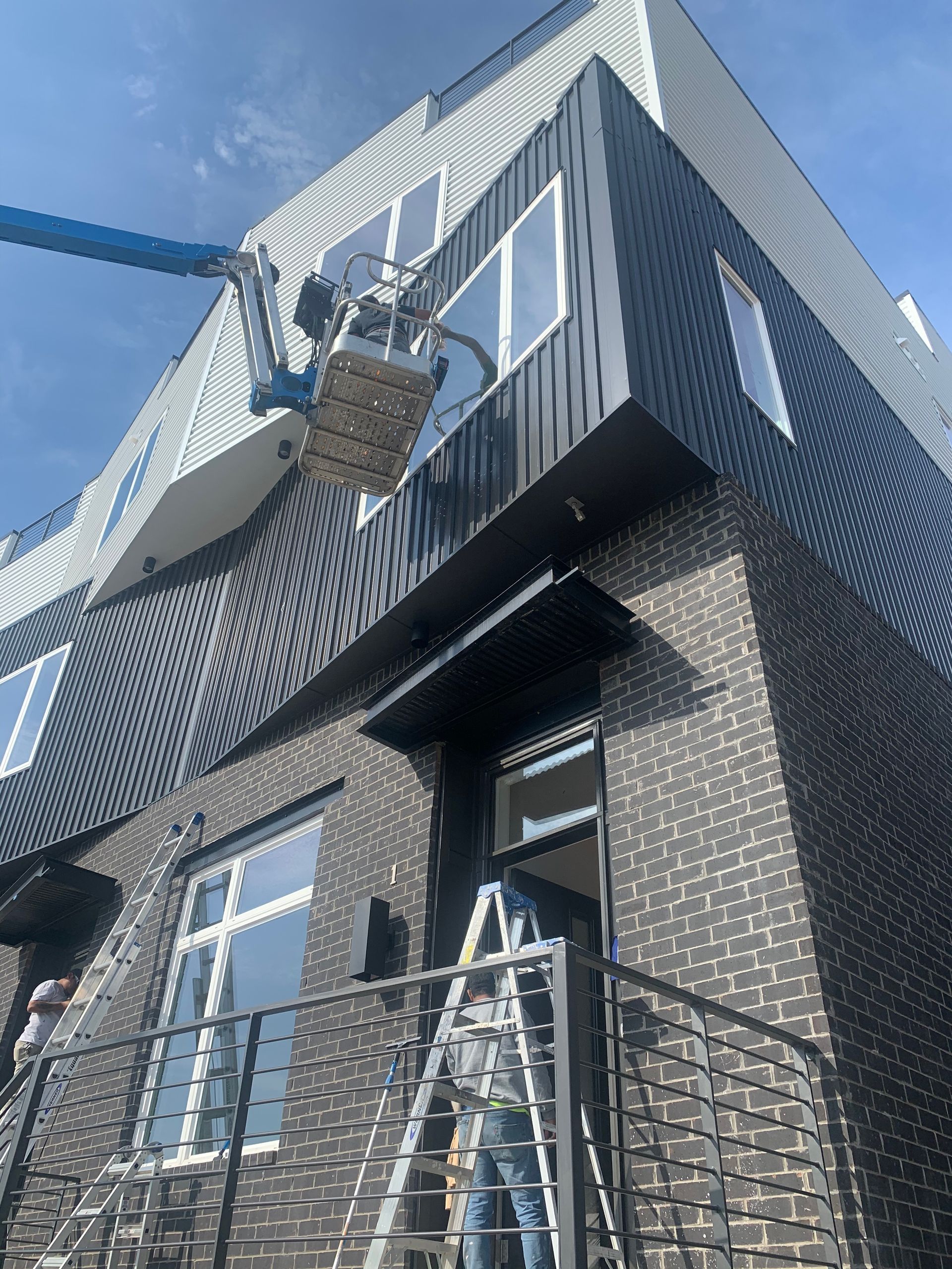 Workers on a lift and ladder working on a modern, dark brick building.