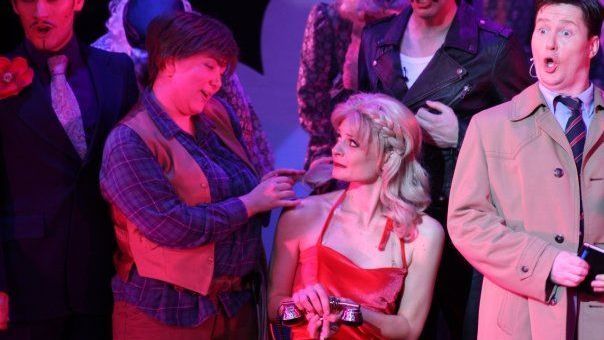 A group of people are standing around a woman in a red dress.