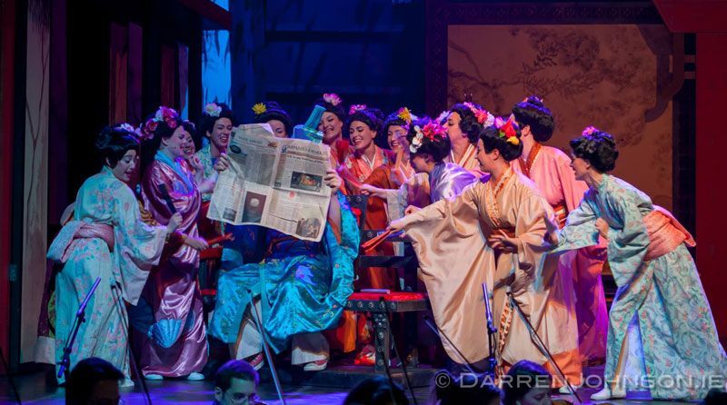 A group of women in kimonos are standing on a stage holding a newspaper.