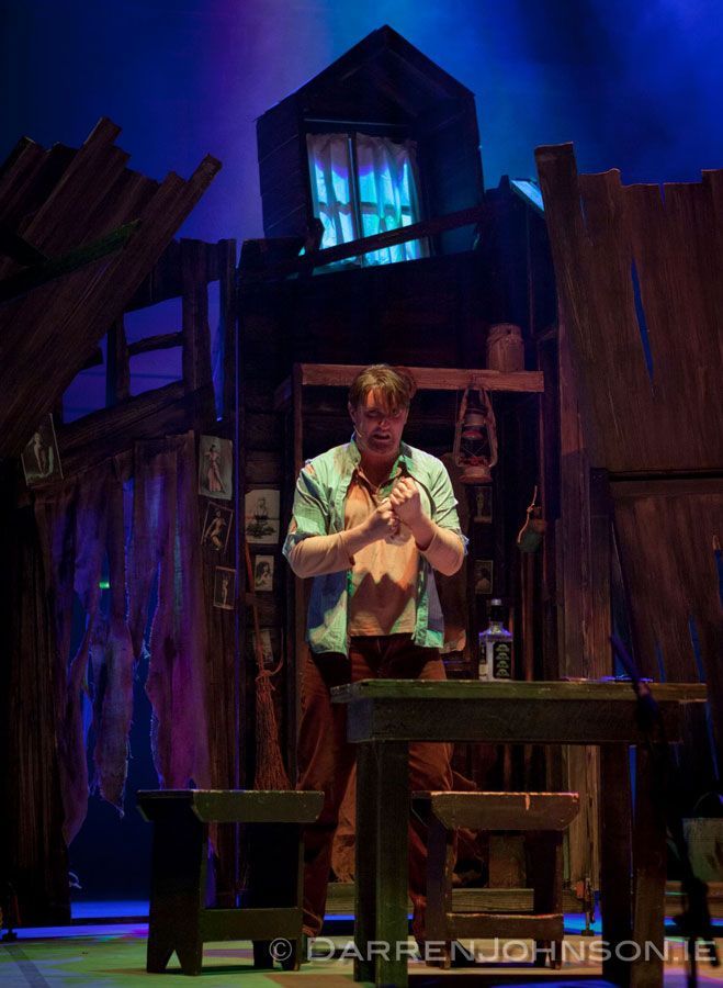A man without a shirt is standing next to a table on a stage.