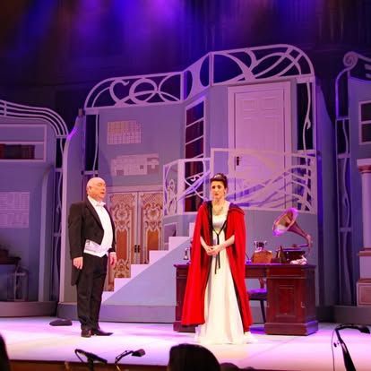 A man and a woman are standing on a stage in front of a building.