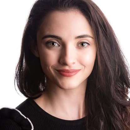 A woman with long brown hair is smiling and wearing a black sweater.