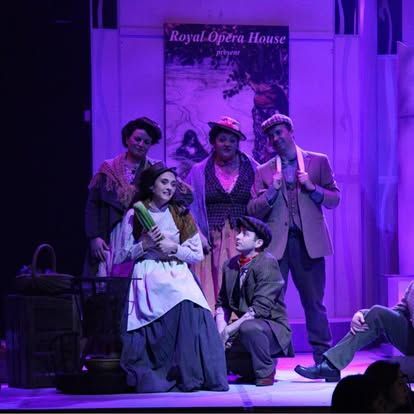 A group of people are standing on a stage in front of a sign that says royal opera house.