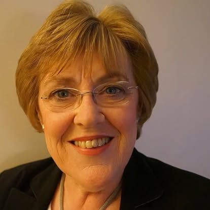 A woman wearing glasses and a black jacket is smiling for the camera.