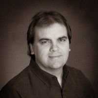 A black and white photo of a man wearing glasses and a polo shirt.