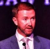 A man in a suit and tie is standing in front of a microphone.