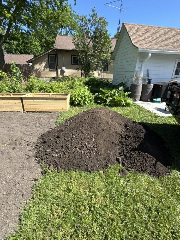 Fresh dark soil piled in a sunny backyard garden beside a house and raised planter box