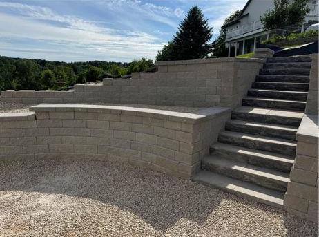 Stone retaining wall and stairs beside a house overlooking a gravel patio and wooded landscape