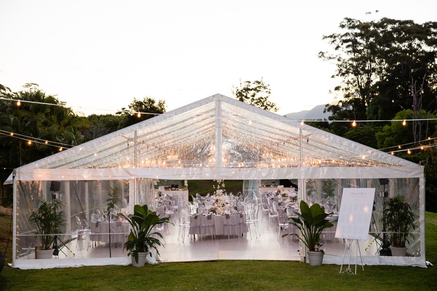 A Clear Tent With Tables And Chairs Inside Of It Is Sitting On Top Of A Lush Green Field — Wedding & Event Hire In Goonellabah, NSW