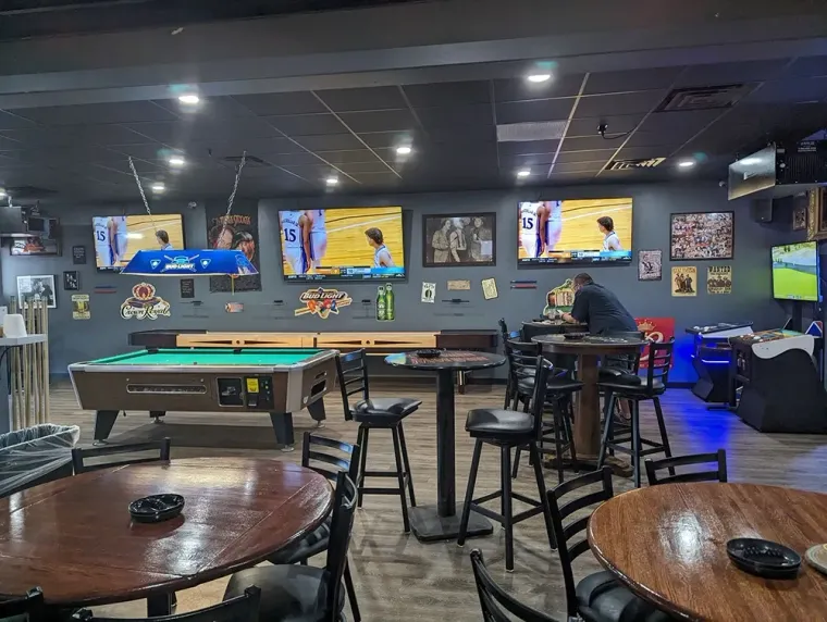 Bar with pool tables, stools, TVs, and neon-lit wall décor in a dimly lit lounge