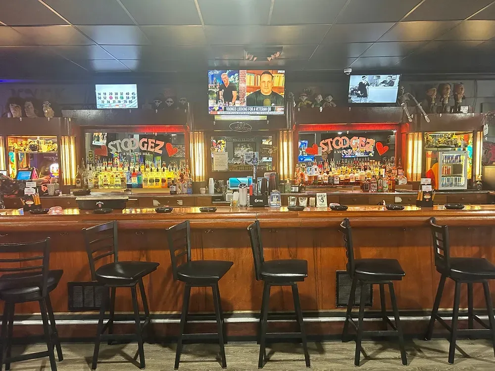 Empty bar interior with stools, wooden counter, and multiple TV screens above the back bar.
