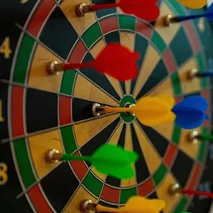 Colorful darts stuck in a dartboard, close-up with red, green, yellow, and blue fletching.