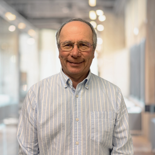 A man in a plaid shirt and glasses is standing in a hallway.