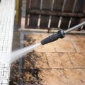 A pressure washer spray cleans dirt off a white tiled pool edge and textured stone patio.