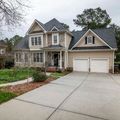 A two-story suburban home with tan siding, stone accents, a dark shingled roof, and a two-car garage at the end of a driveway