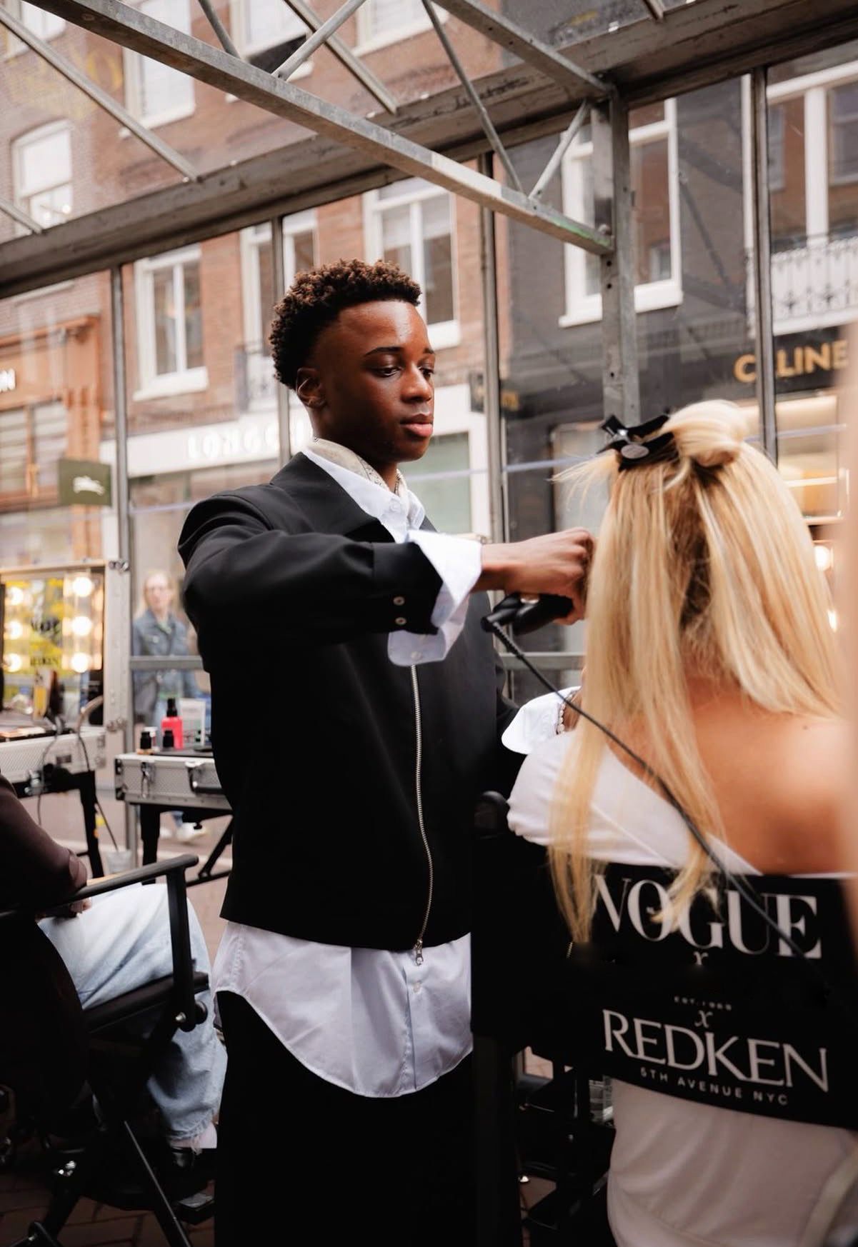 Een kapper knipt het haar van een klant in een salon, waar spiegels en stoelen zichtbaar zijn.