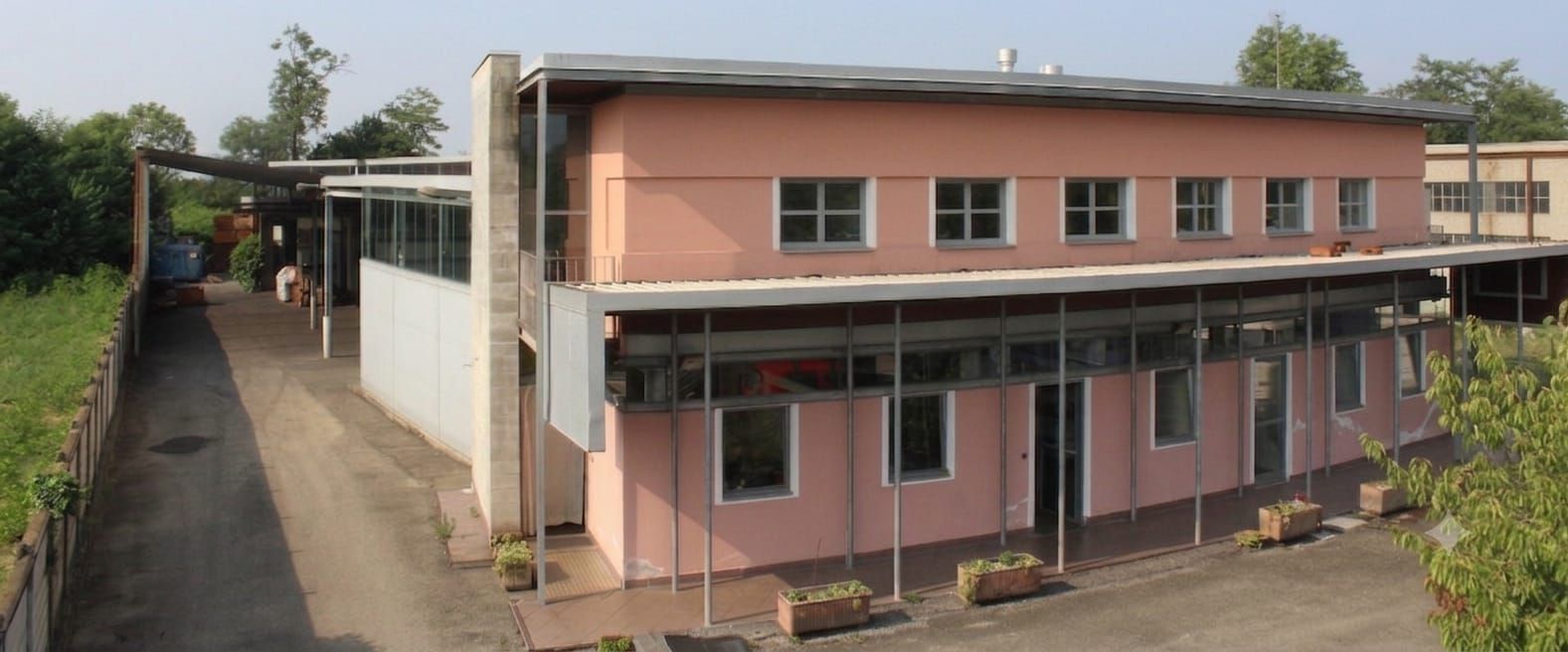 Edificio rosa a due piani con passaggio coperto accanto a uno stretto vialetto e vegetazione.