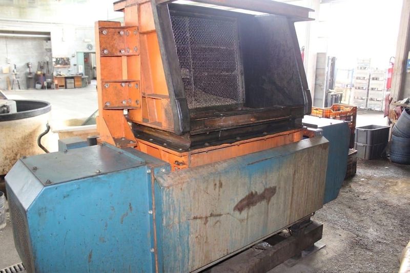 Macchina industriale con involucro arancione e blu in un'officina, aperta per mostrare i rulli interni