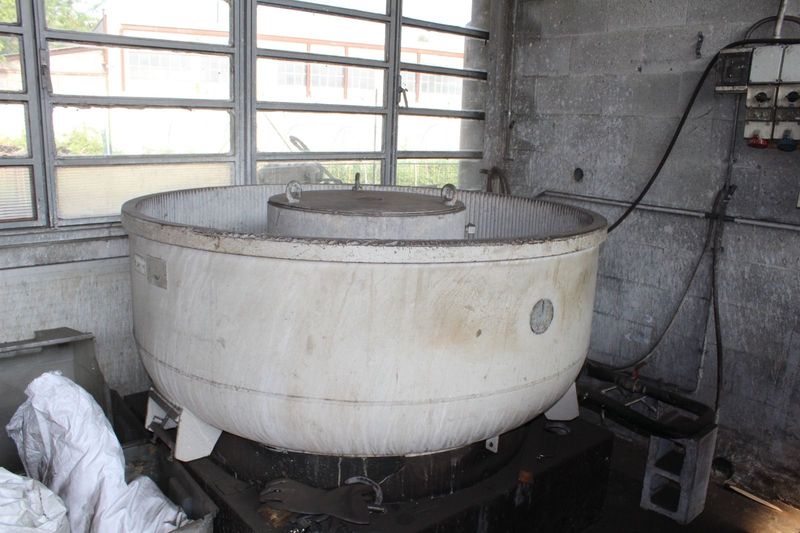 Un grande miscelatore industriale bianco in una stanza di cemento consumato con finestre e tubature a vista.