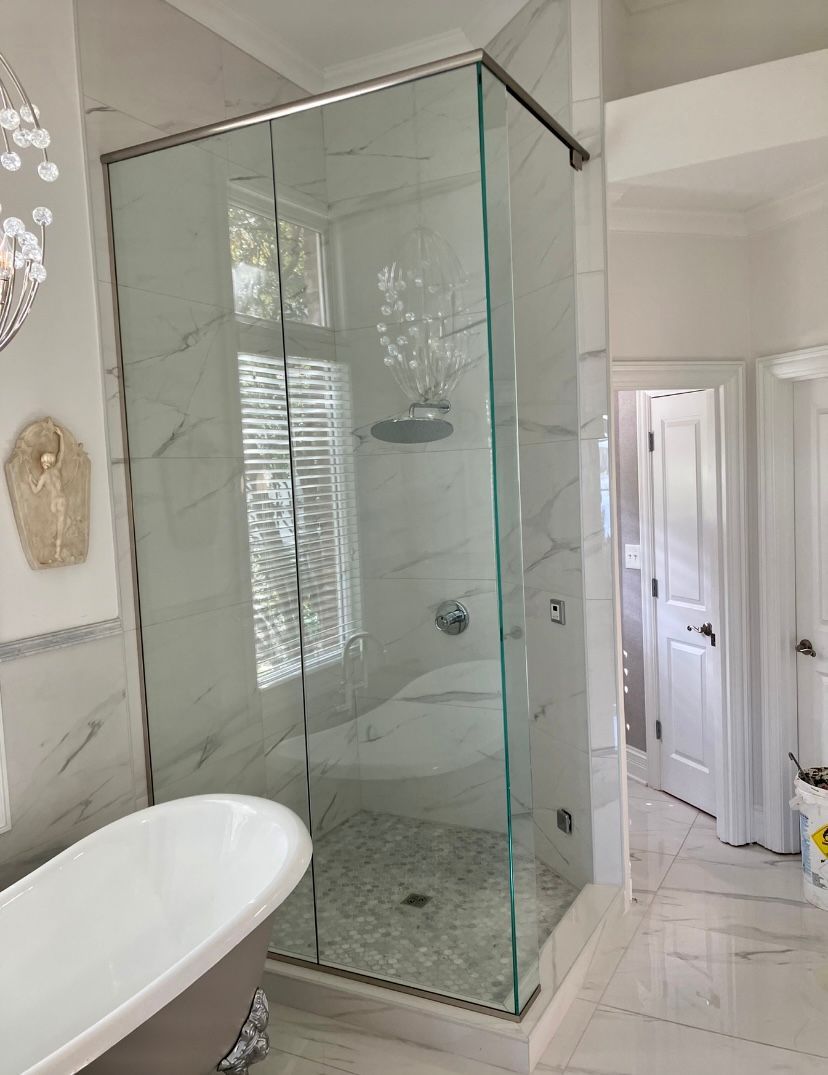 A modern bathroom featuring a white claw-foot tub and a glass-enclosed corner shower with marble-style tile walls.