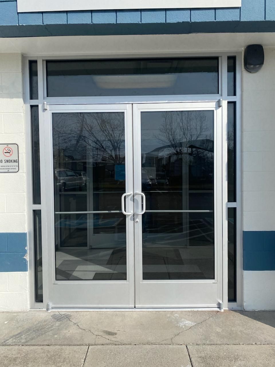 Double glass commercial entrance doors with silver frames set into a white and blue concrete block building.