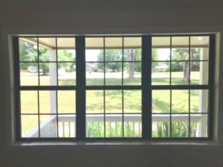 A dark-framed, multi-pane window looking out onto a grassy lawn and a porch with white railings.