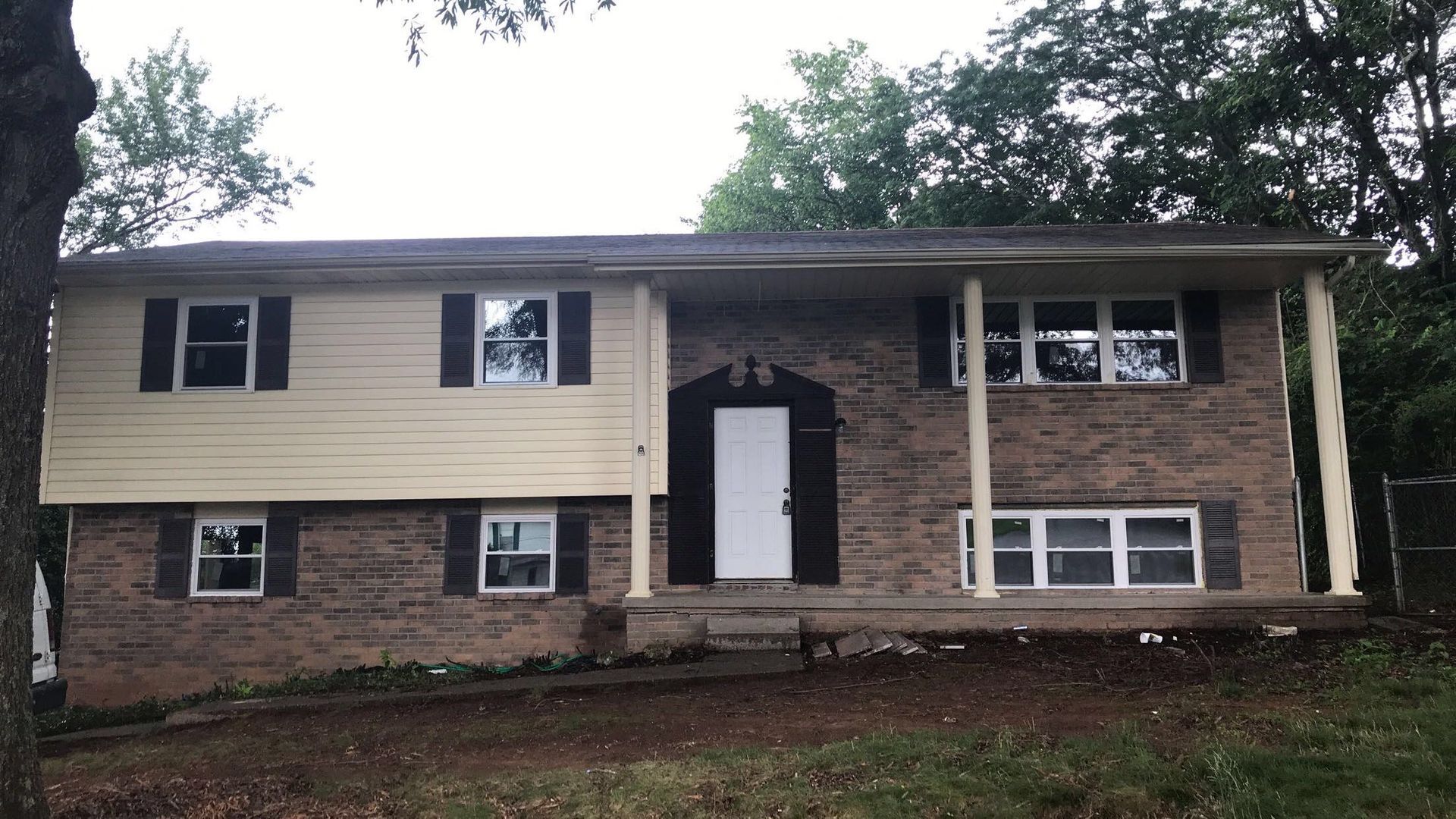 A two-story split-level home featuring beige siding on the left, stone masonry on the right, and a white front door.