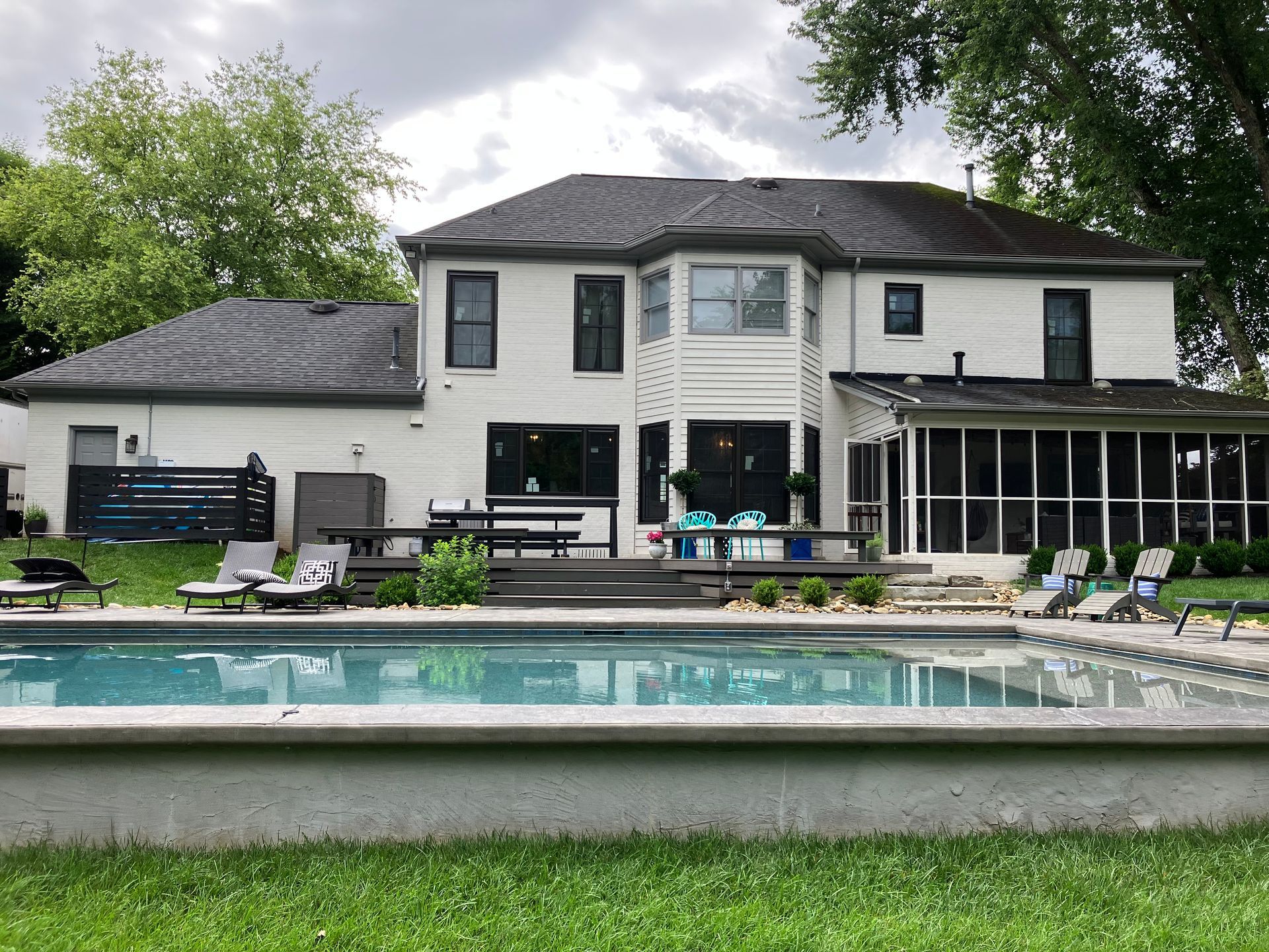 A two-story white house with a swimming pool in the foreground, wooden deck, and a screened-in porch on the right side.