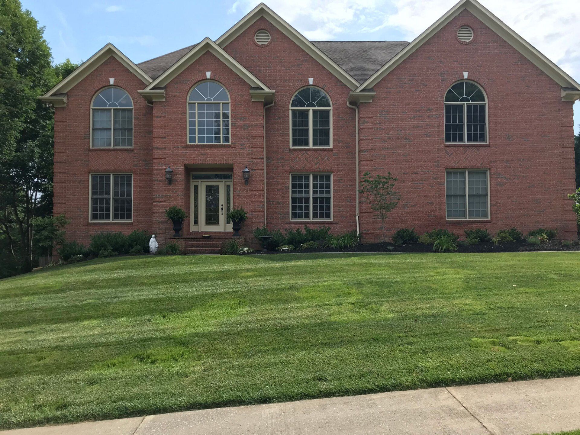 A two-story red brick house with a front door, arched windows, and a well-maintained lawn under a clear sky.